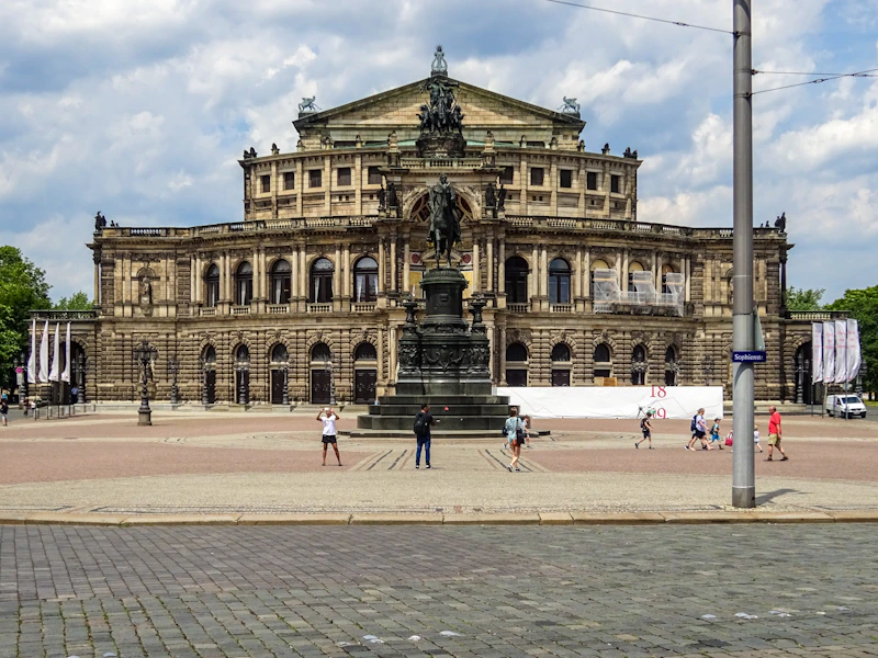 Grand opera house with a monument in front.