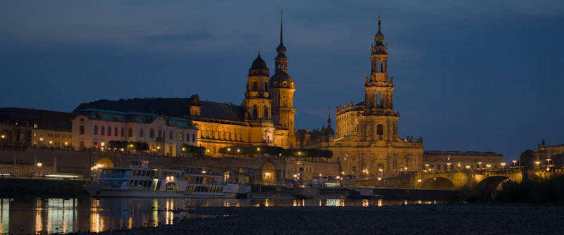 Illuminated historic buildings along a river at dusk